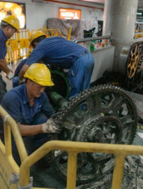 Workers in hard hats repair large industrial machinery gears.